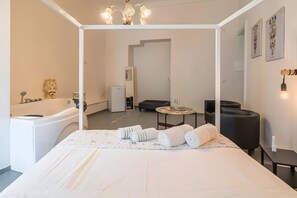 A modern hotel room with a large bed, a bathtub, a small table, and a chair.