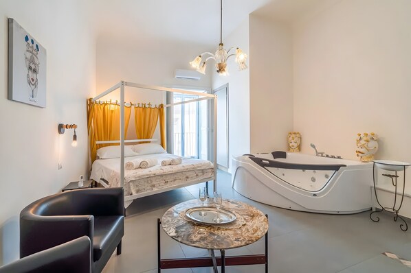 A modern hotel room with a four-poster bed, a bathtub, a round table with a tray, and a small side table.