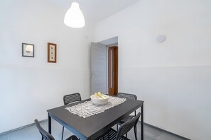 A dining area with a table, chairs, a bowl with lemons, a white lace table runner, and a pendant light.