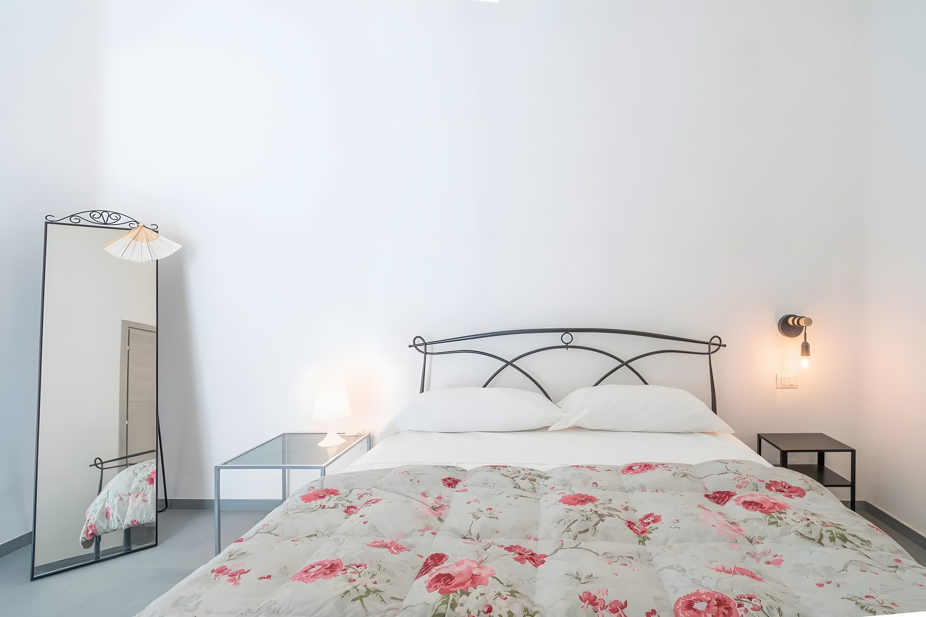 Ein Schlafzimmer mit Bett, Spiegel, Nachttisch und Wandleuchte.