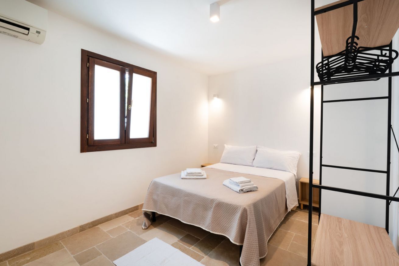 Une chambre à coucher comprenant un lit, une fenêtre, un climatiseur fixé au mur et un étagère en métal.