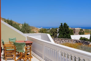 Un balcon avec une table et des chaises, donnant sur un paysage côtier avec des bâtiments et des arbres.