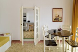 Un coin repas avec une table ronde, des chaises, un saladier de fruits et un tableau accroché au mur.