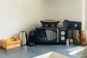 Une cuisine équipée d’un four à micro-ondes, d’une bouilloire, d’une machine à café et de divers ustensiles de cuisine disposés sur le plan de travail.