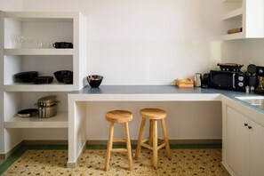 A kitchen with white cabinetry, a granite countertop, two wooden stools, and various kitchen appliances. - Two Bedroom Villa with Sea View, Kaminia Holiday Homes (Santorini)