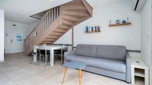 A modern living room with a grey sofa, a small round table, a wooden staircase, and a dining area with chairs and a table. - Charming Villa by Serignan Beach (Sérignan)