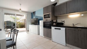 A modern kitchen with grey cabinets, a built-in oven, microwave, and dishwasher. There is a dining area with a table and chairs visible through a glass door. - Charming Villa by Serignan Beach (Sérignan)