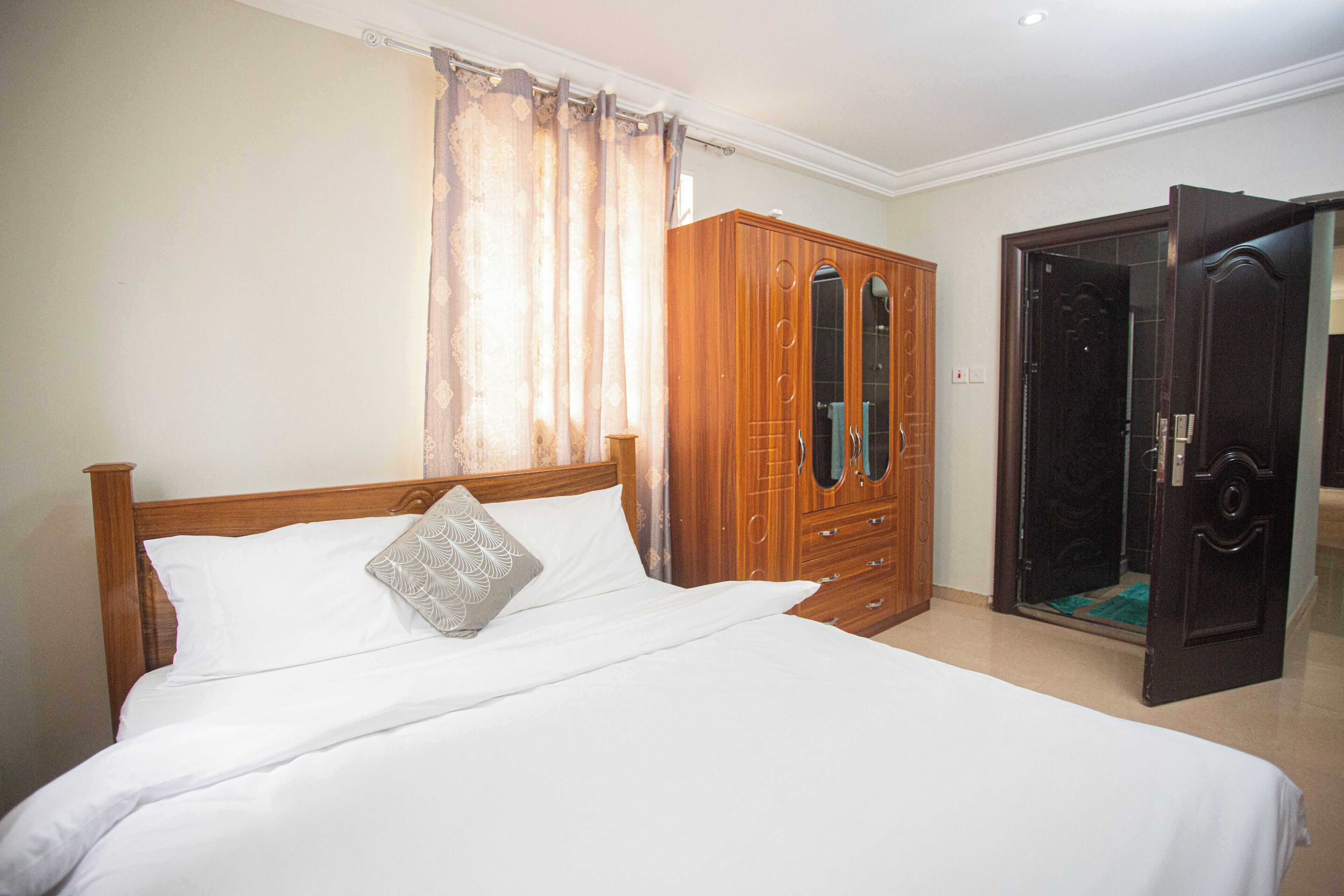 Une chambre à coucher avec un lit en bois, une armoire et une porte ouverte donnant sur une salle de bain.