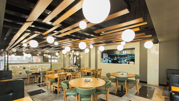 Un restaurant avec des tables rondes, des chaises vertes et des luminaires suspendus.