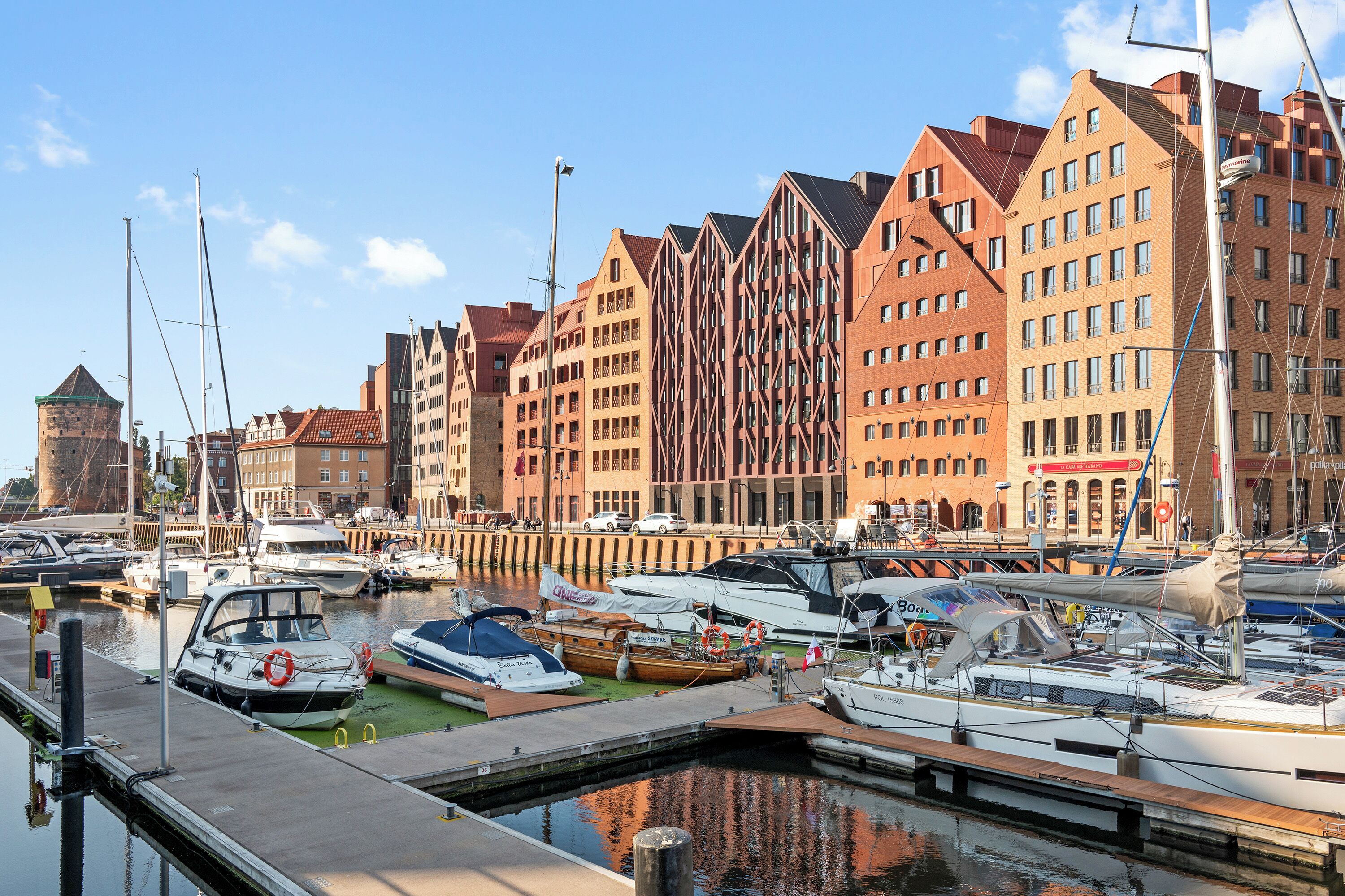 Ein Yachthafen mit verschiedenen Booten an den Stegen, umgeben von Gebäuden unterschiedlicher Architektur.