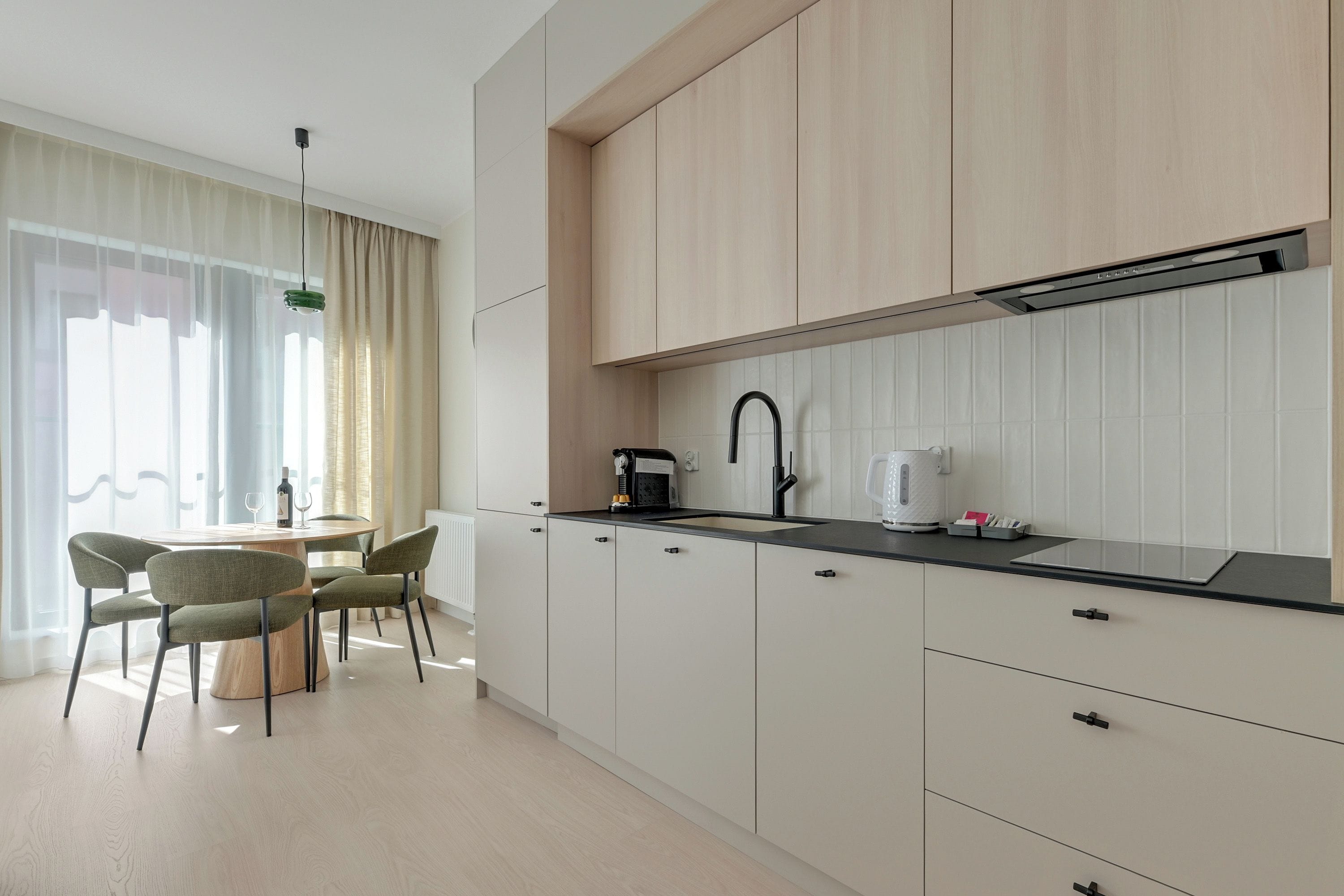 A modern kitchen with a black countertop, white cabinets, and a dining area with a round table and chairs.
