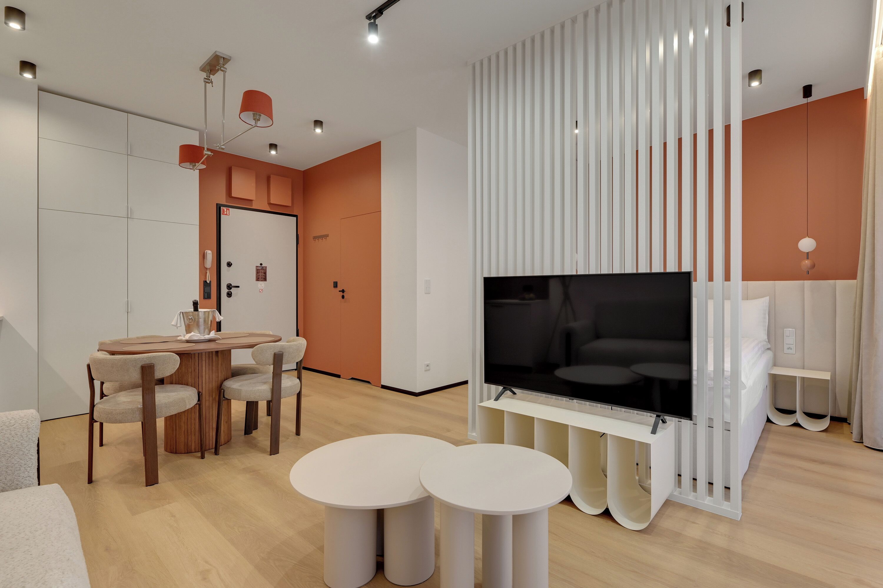 Ein modernes Wohnzimmer mit Fernseher, Esstisch mit Stühlen und einer weißen Trennwand mit vertikalen Lamellen.