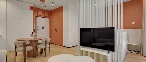 Ein modernes Wohnzimmer mit Fernseher, Esstisch mit Stühlen und einer weißen Trennwand mit vertikalen Lamellen.