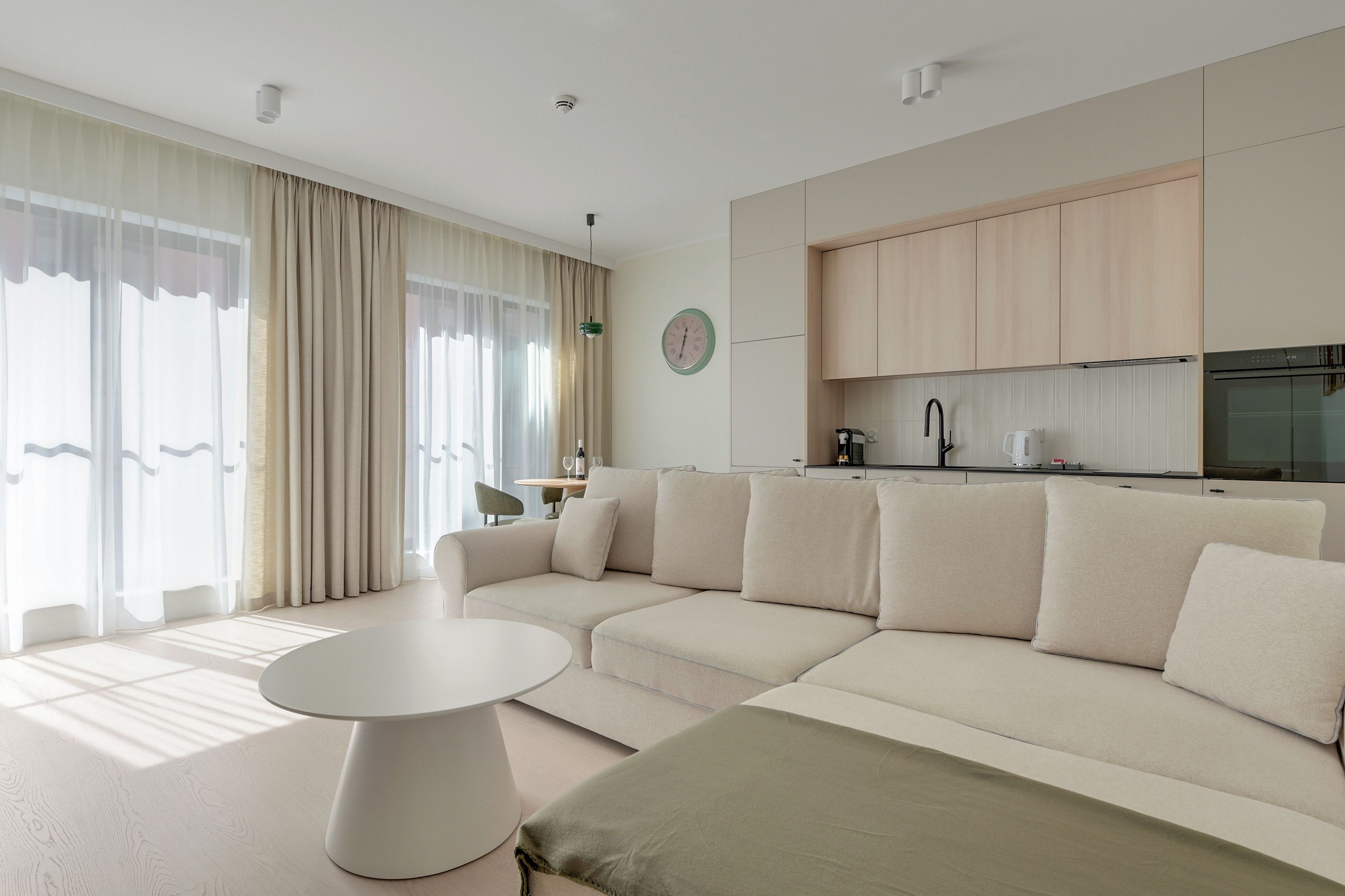 A modern living room with a sectional sofa, a round coffee table, and a dining area with a kitchen in the background.