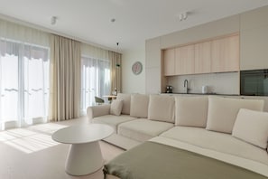 A modern living room with a sectional sofa, a round coffee table, and a dining area with a kitchen in the background. - GRANO APARTMENTS Gdańsk Granaria (Gdańsk)