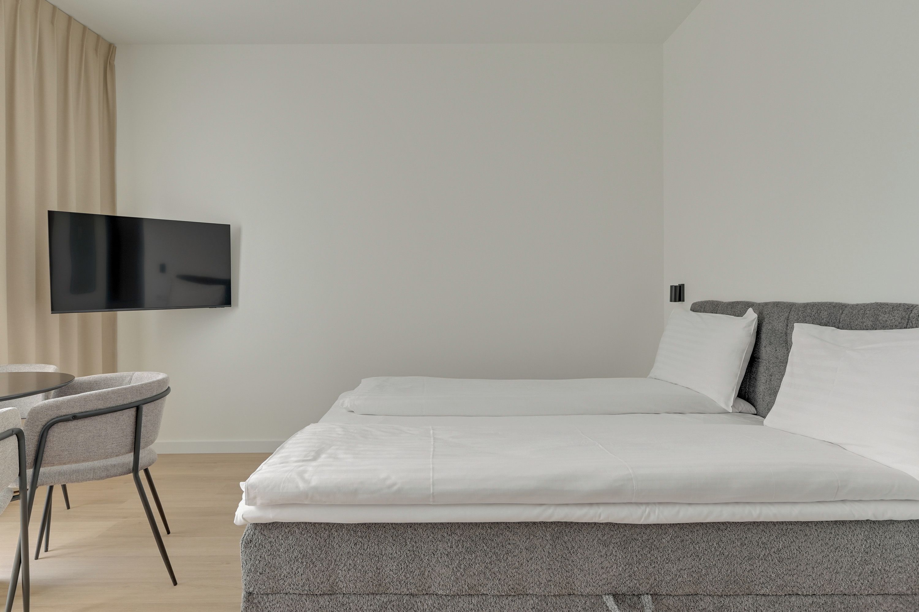 A hotel room with a bed, a TV mounted on the wall, a small table, and two chairs.