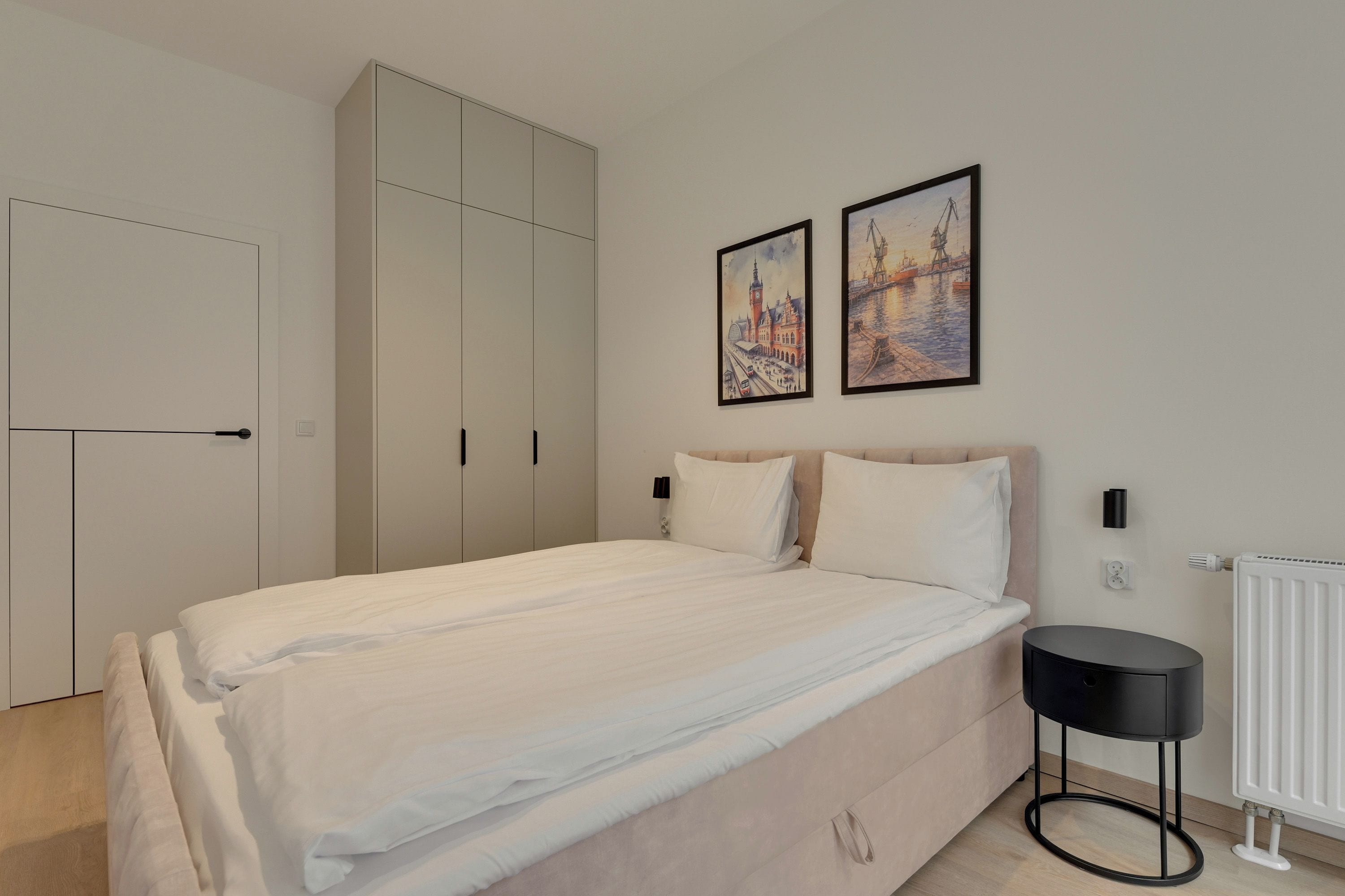 Ein Schlafzimmer mit einem Bett, einem Kleiderschrank, einem Heizkörper und zwei gerahmten Bildern an der Wand.