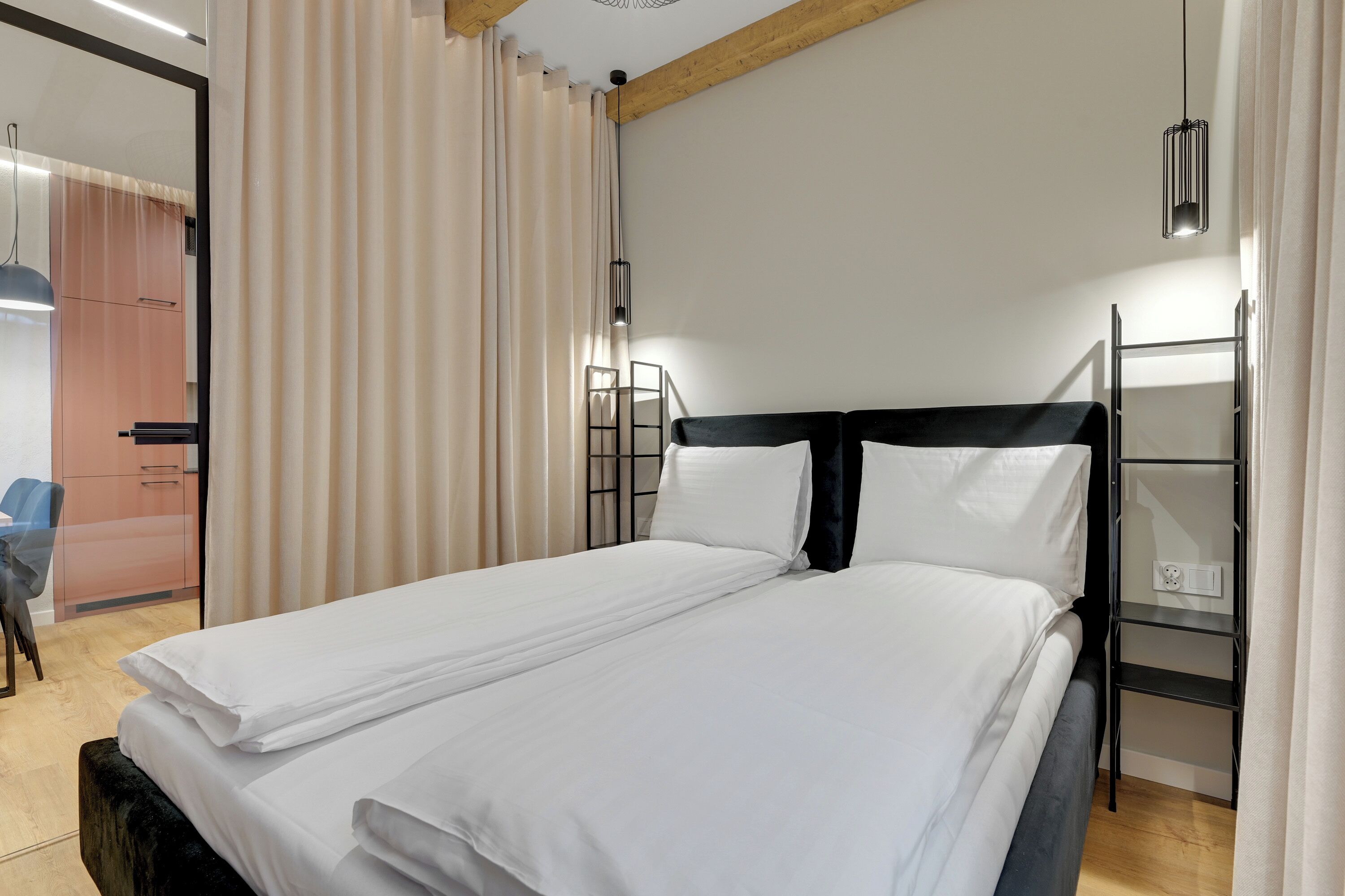 A neatly made bed with white linens, a black headboard, and a bedside shelf with a power outlet.