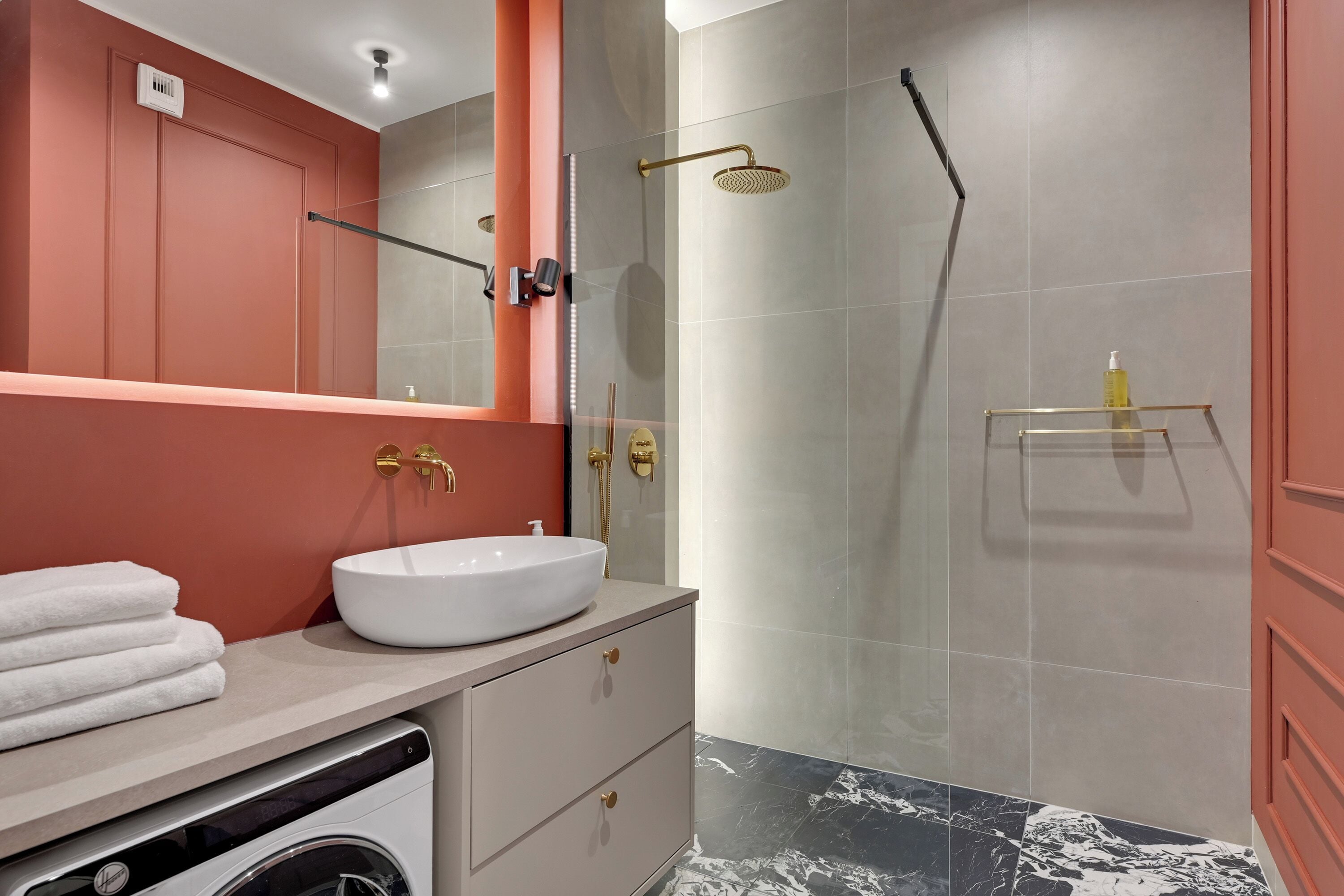 A modern bathroom with a white sink, a washing machine, and a glass-enclosed shower area.