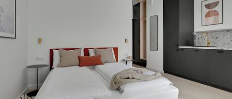 Una habitación de hotel moderna con una cama grande, una mesita de noche pequeña, un armario empotrado y una zona de kitchenette.
