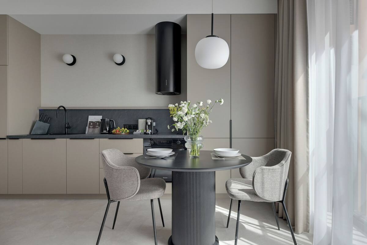 Una cucina moderna con un tavolo da pranzo rotondo, sedie grigie e un vaso di fiori bianchi.
