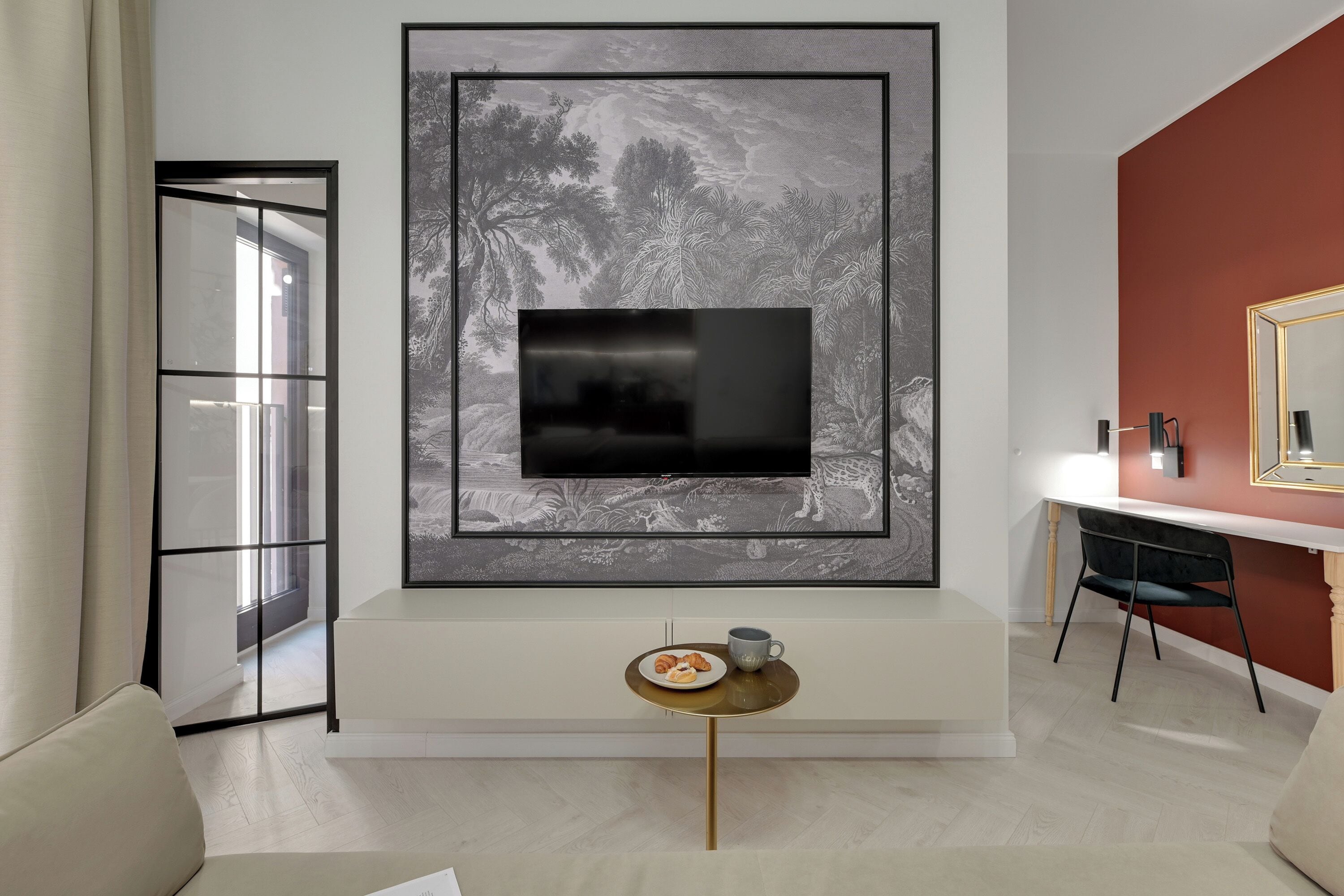 Uma sala de estar moderna com uma televisão grande fixada na parede, uma mesinha redonda com um prato de comida e uma cadeira.