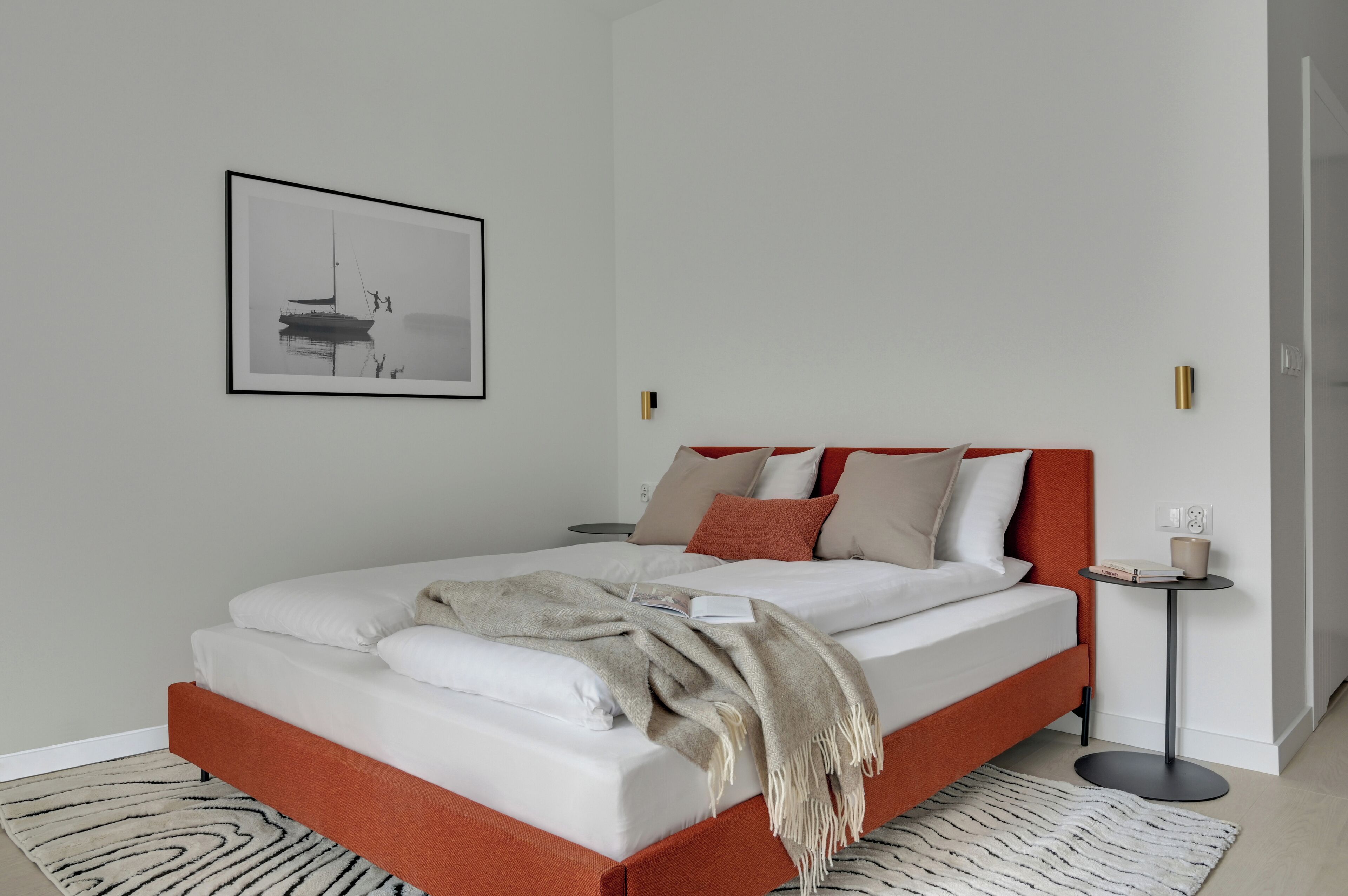 A modern bedroom with a bed, a side table, a framed picture, and a rug.