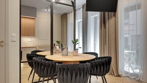 A modern dining area with a round table, six upholstered chairs, and a view of the kitchen and balcony through a glass partition. - GRANO APARTMENTS Gdańsk Granaria (Gdańsk)