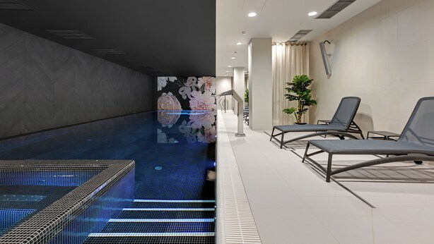 A modern indoor pool area with a tiled floor, lounge chairs, and a wall with a floral mural. - GRANO APARTMENTS Gdańsk Granaria (Gdańsk)