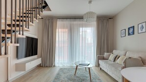 A modern living room with a staircase, a flat-screen TV, a sofa, a coffee table, and a patterned rug. - GRANO APARTMENTS Gdańsk Granaria (Gdańsk)
