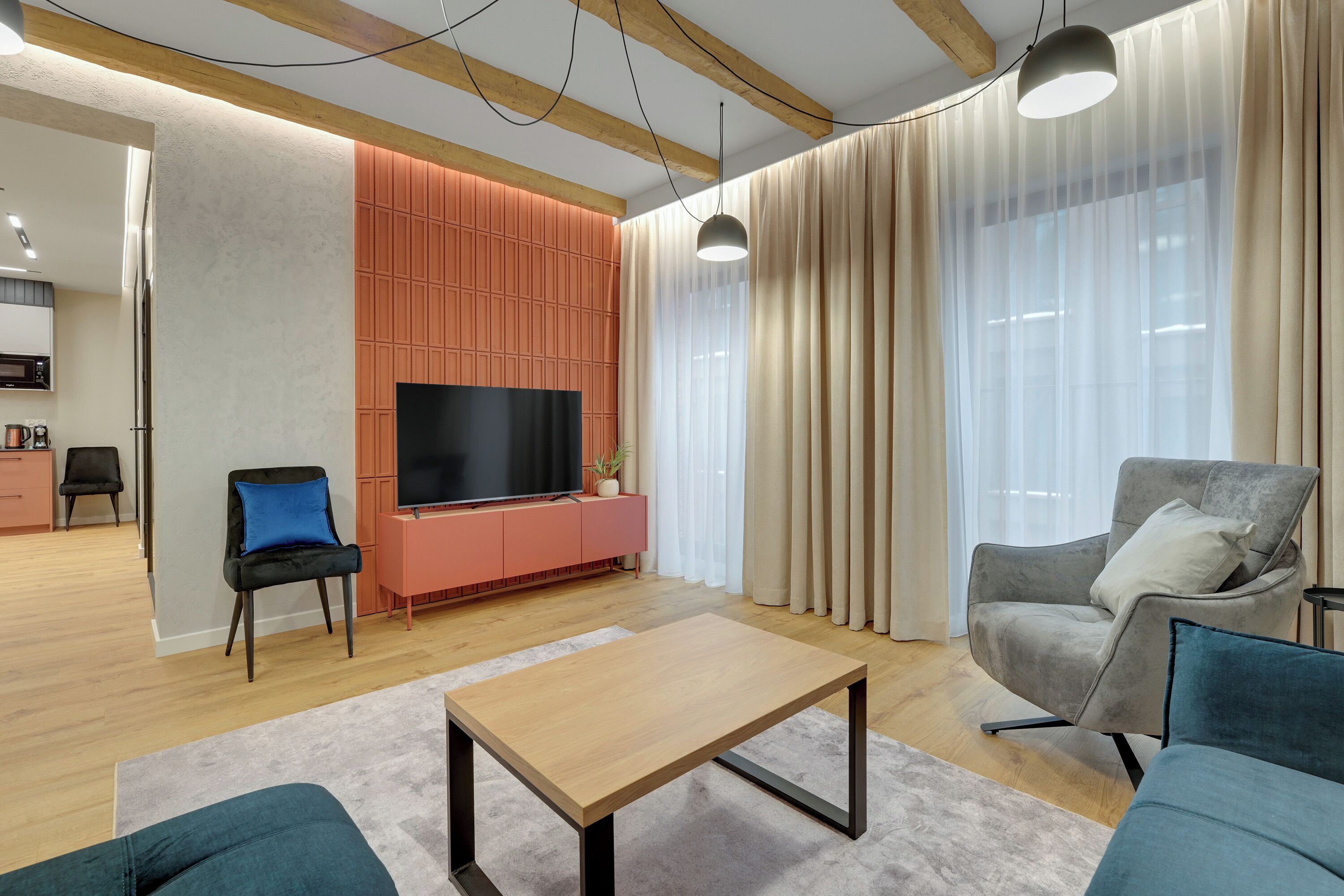 A modern living room with a flat-screen TV, a wooden coffee table, and a grey armchair.