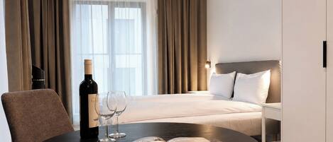 A hotel room with a bed, a table with a bottle and glasses, and a magazine.