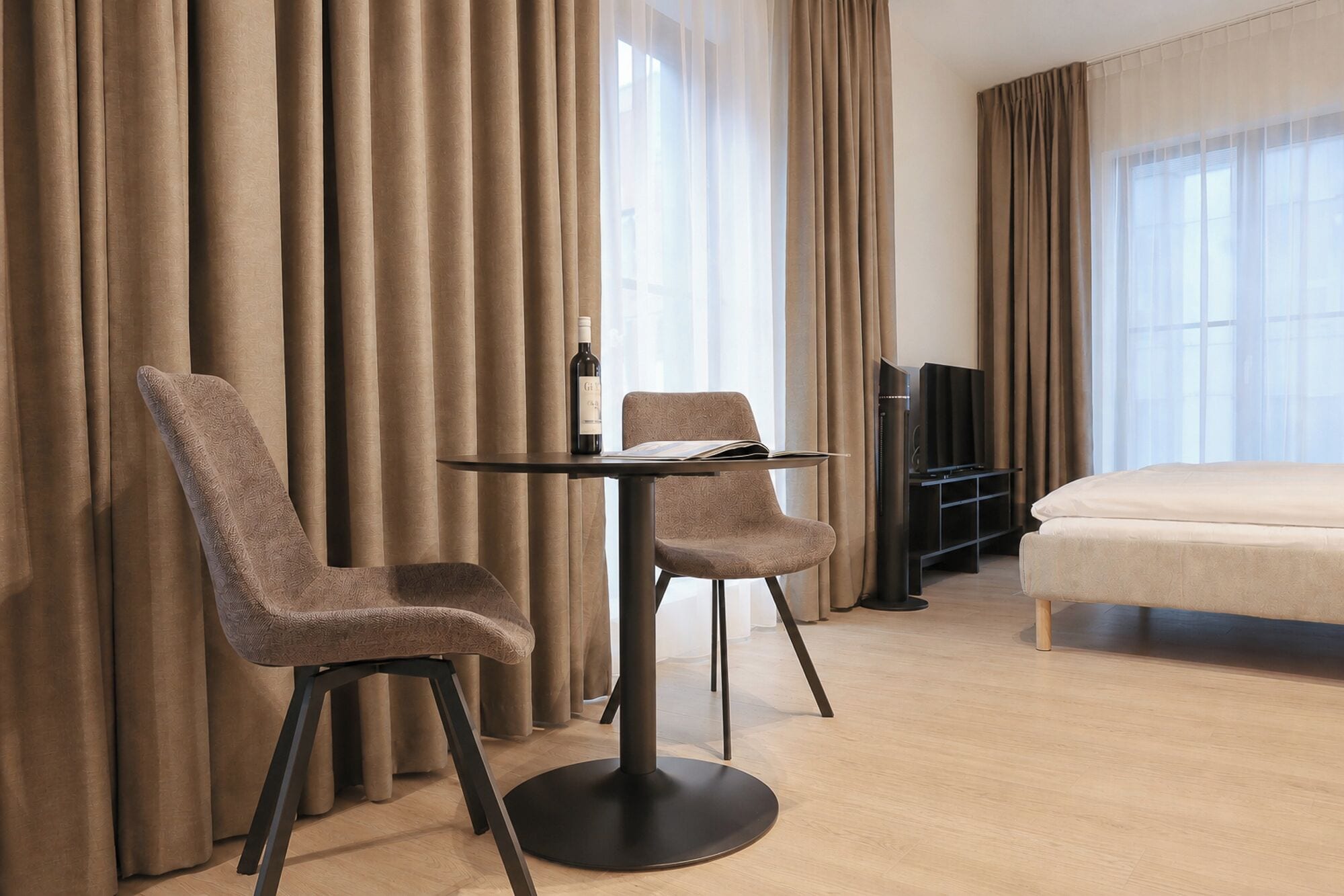 Habitación de hotel con cama, televisión, una mesa y dos sillas, y cortinas.