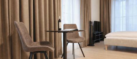 A hotel room with a bed, a TV, a table with two chairs, and curtains.