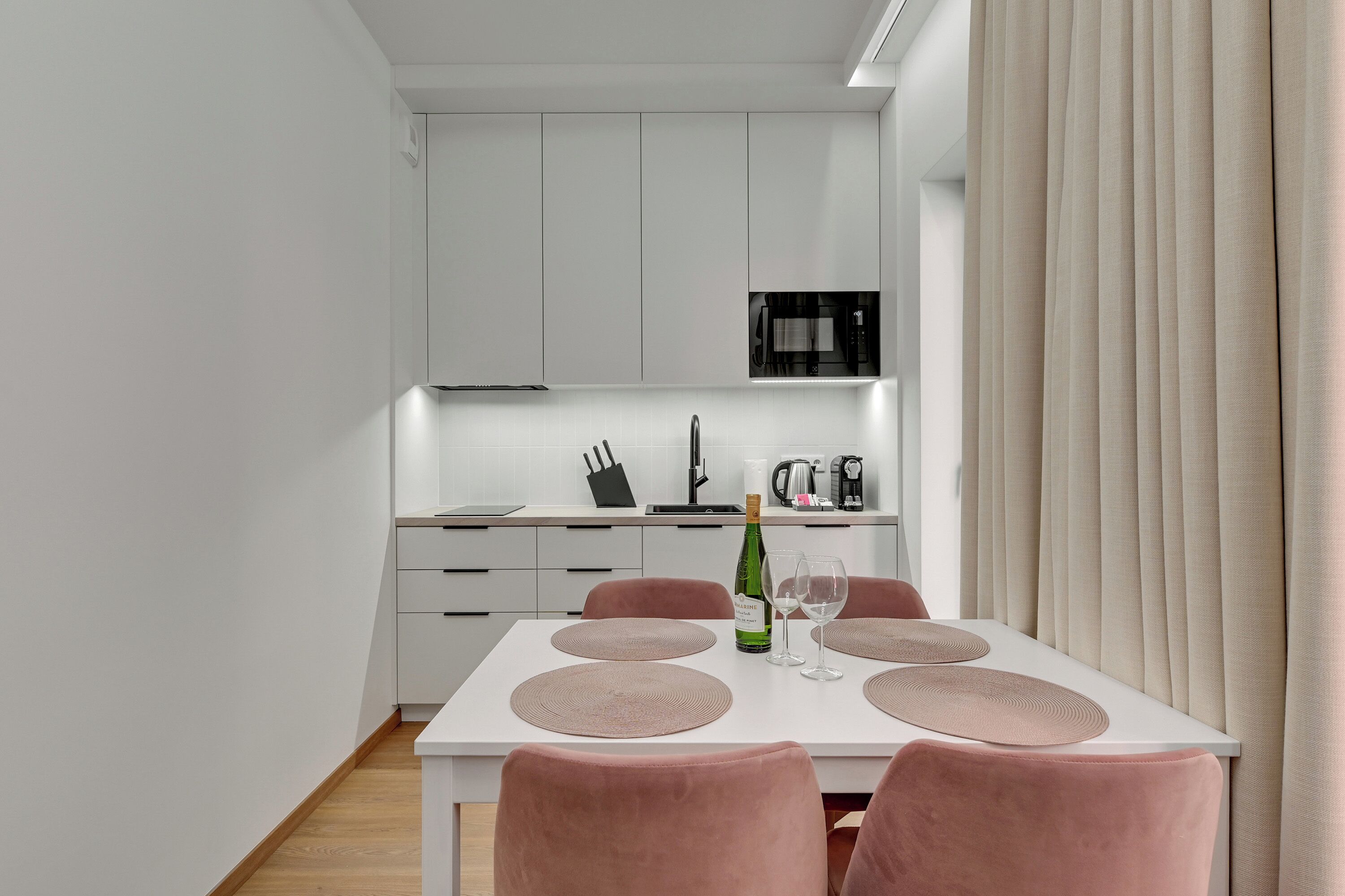 Een moderne keuken met witte kasten, een wit aanrecht en een eettafel met roze stoelen.