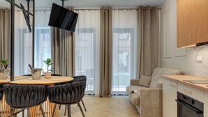 A modern living room with a sofa, a dining table with chairs, and a kitchen area with cabinets and a TV. - GRANO APARTMENTS Gdańsk Granaria (Gdańsk)
