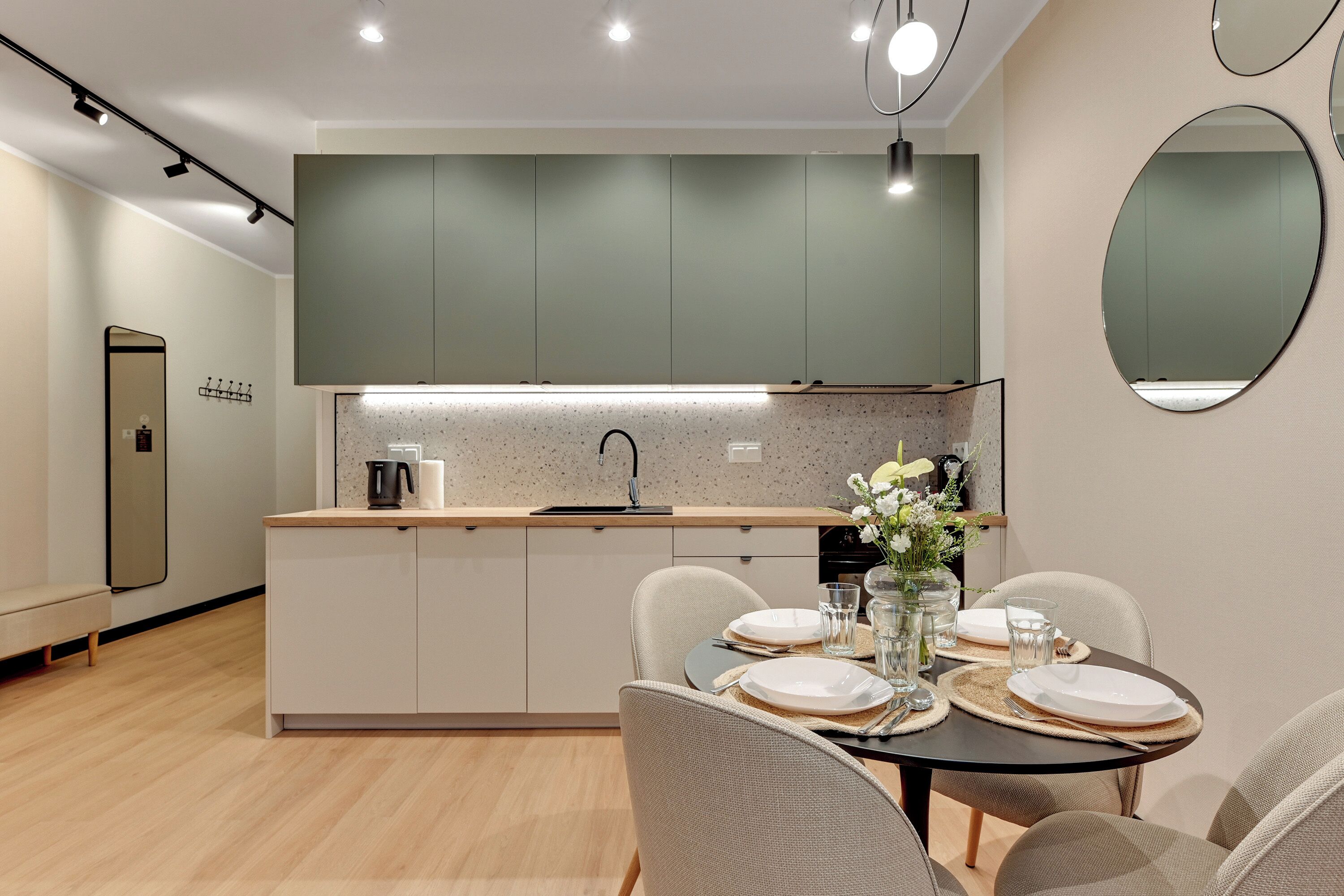 A modern kitchen with a central island, a dining area with a table set for two, and a large mirror on the wall.