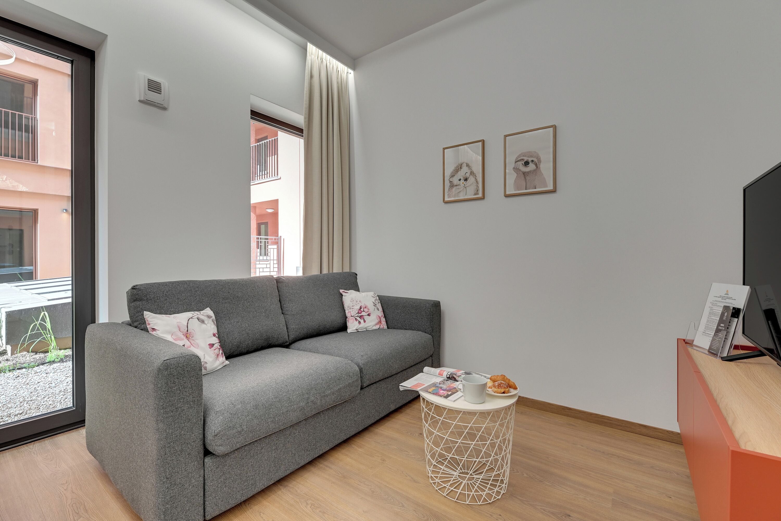 A modern living room with a grey sofa, a small round side table, and two framed pictures on the wall.