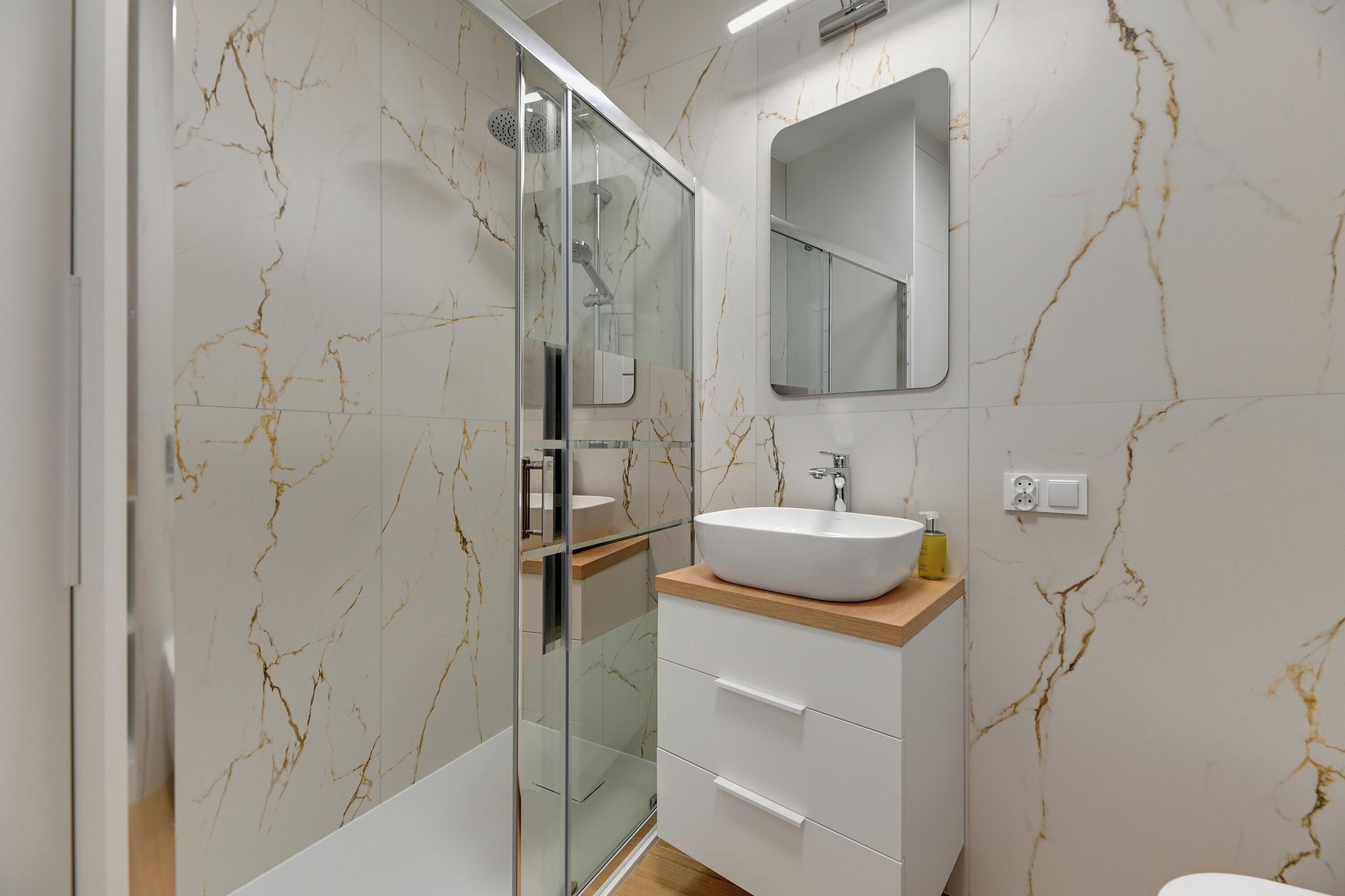 Une salle de bain moderne avec une douche à parois de verre, un lavabo blanc doté d’un plan de travail en marbre et un miroir au-dessus du lavabo.