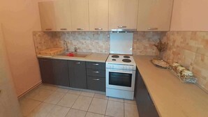 A compact kitchen with dark cabinets, a white stove, and a tiled backsplash. - The Cottage in Paralia (Paralia)