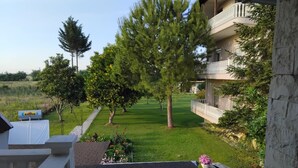 A view from a balcony overlooking a well-maintained lawn with trees and a building with a balcony. - The Cottage in Paralia (Paralia)