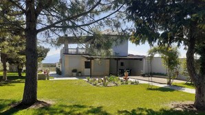 A two-story building with a balcony, surrounded by a well-maintained lawn and trees. - The Cottage in Paralia (Paralia)