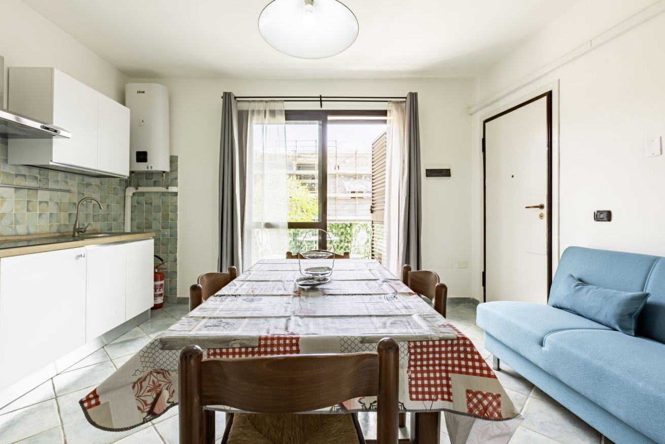 A dining area with a table set for six, a blue sofa, and a kitchen with white cabinets and a tiled backsplash.