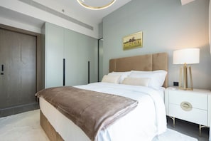A modern bedroom with a large bed, a bedside table with a lamp, and a wardrobe.