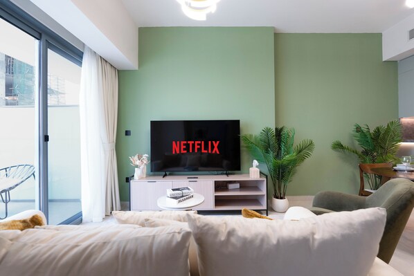A modern living room with a large flat-screen TV, a sofa, and a dining area with a table and chairs.