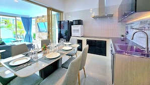 A modern kitchen with a dining area, featuring a built-in oven, microwave, and a sink with a faucet. - Lux Sila Pool Villa 3 Bedrooms 4 Beds (Koh Samui)