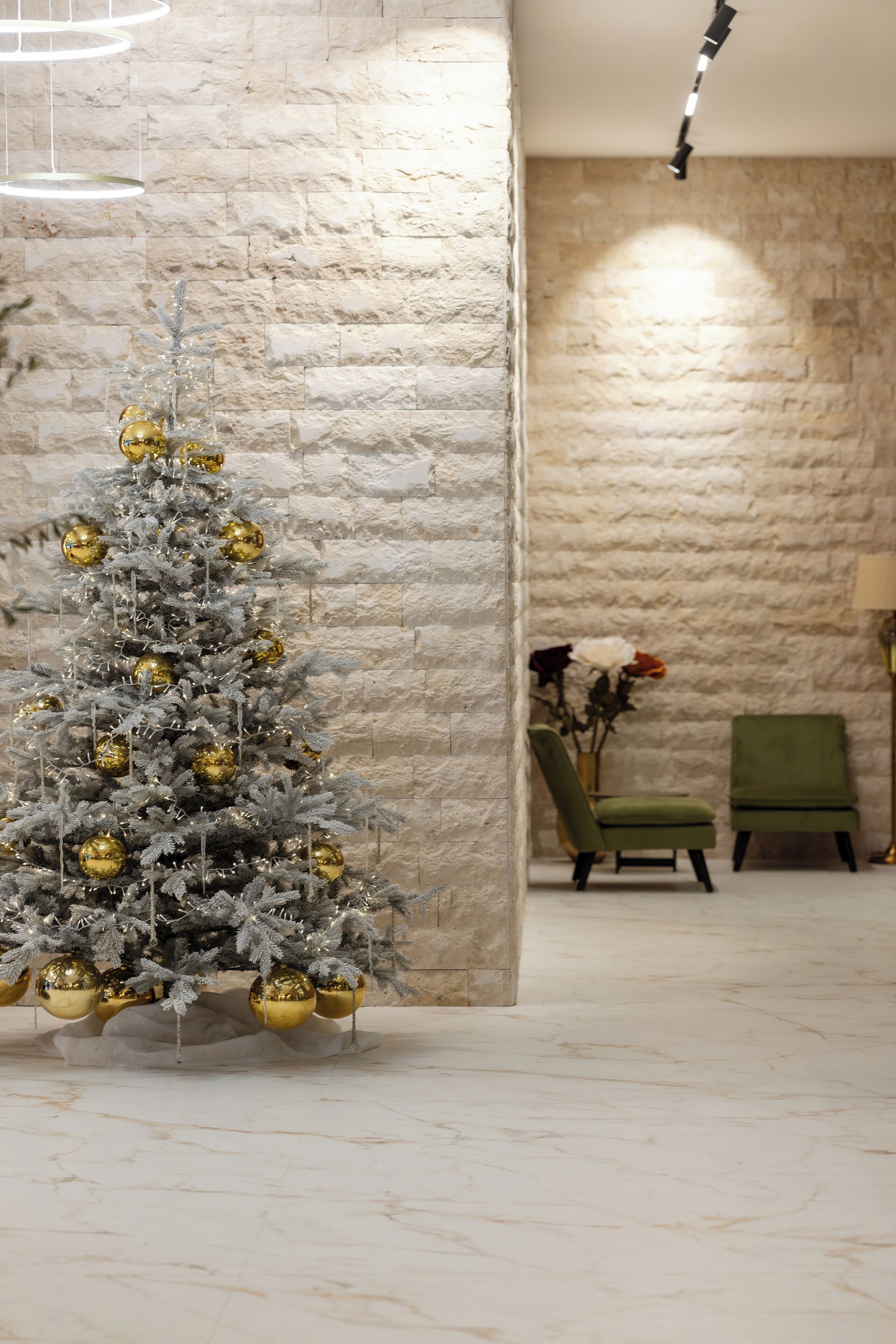 Un sapin de Noël décoré d’ornements dorés, dans une pièce dont un mur est en pierre et où se trouvent des chaises vertes.