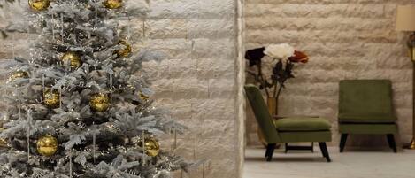 A Christmas tree with gold ornaments in a room with a stone wall and green chairs.
