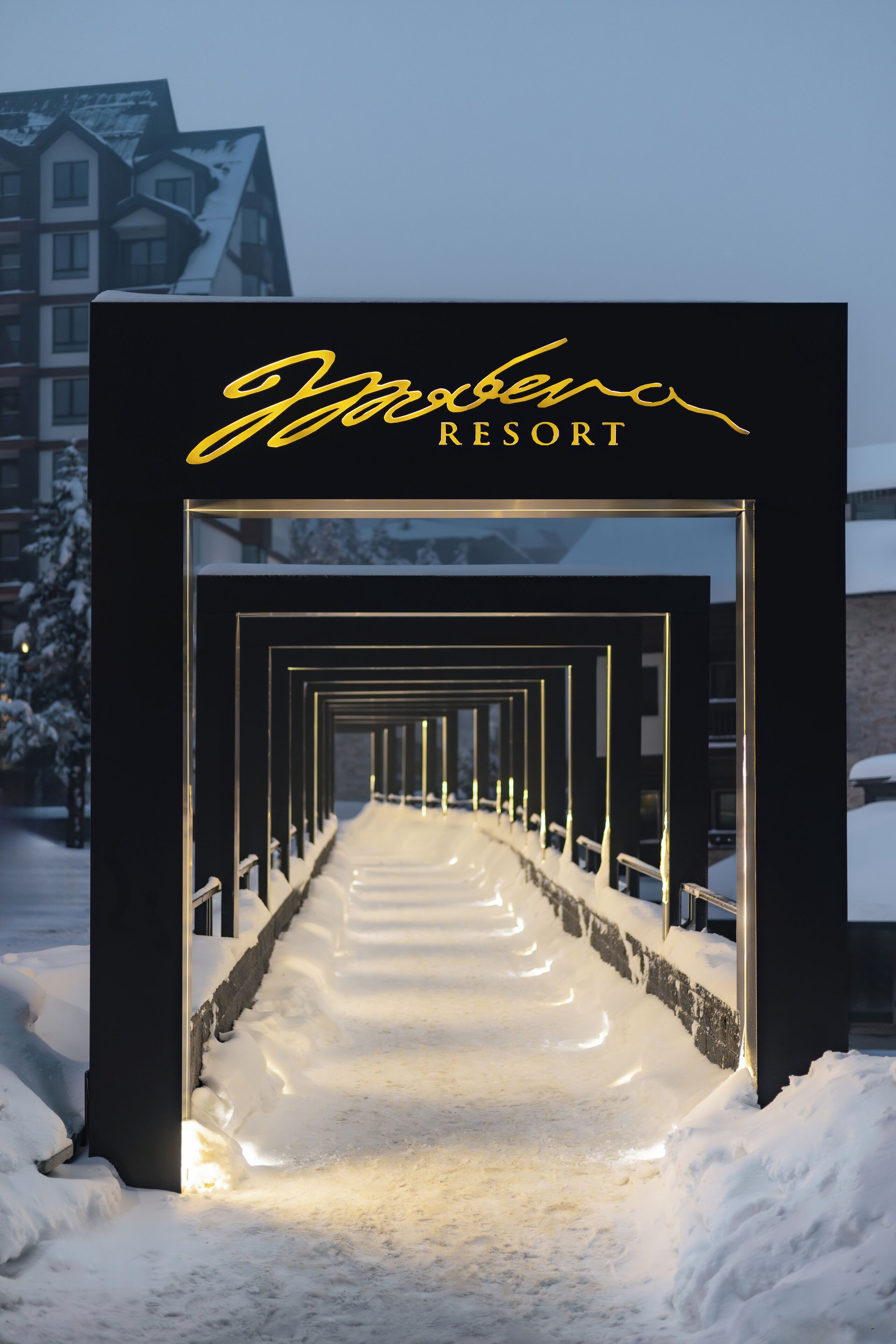 A snow-covered pathway leading to a building with a sign that reads "Yazbeka RESORT".