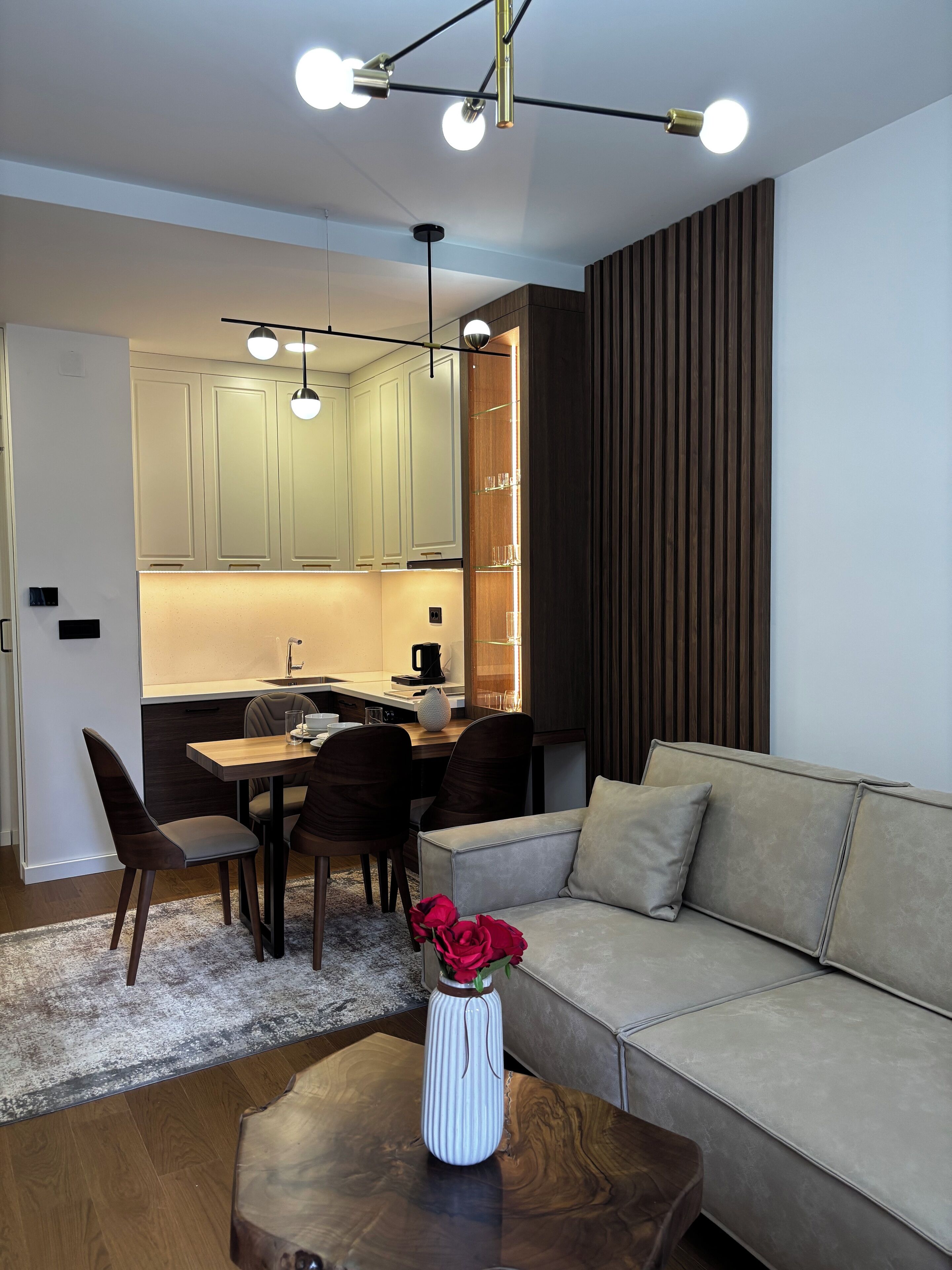 Una cocina moderna con armarios de tonos claros, una zona de comedor con una mesa y sillas de madera, y una sala de estar con un sofá y una mesa de centro.